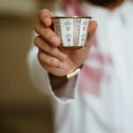 Close-up of Middle Eastern man in traditional attire offering a decorative cup of coffee.